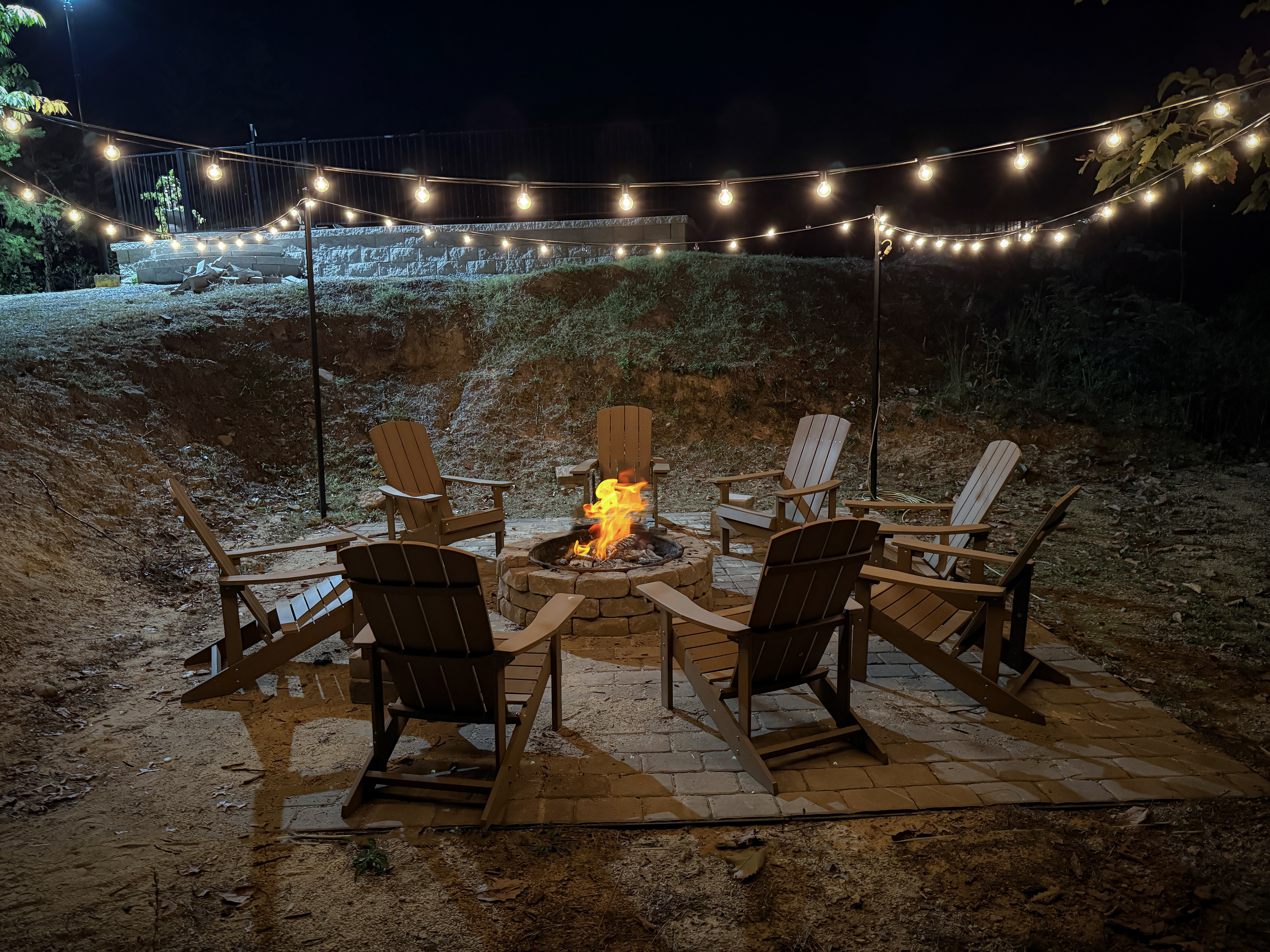 Fire pit surrounded by Adirondack chairs beneath glowing string lights