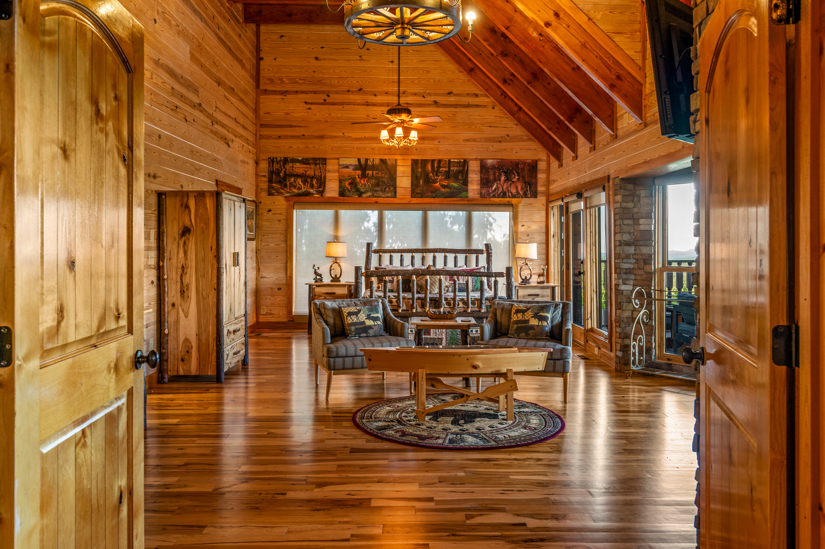 Spacious lodge bedroom with a log bed, vaulted wood ceiling, sitting area, and deck access